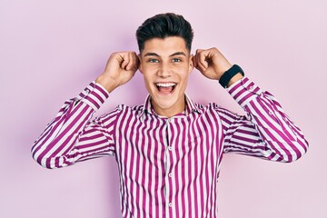 Young hispanic man wearing casual clothes smiling pulling ears with fingers, funny gesture....