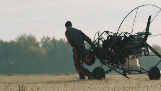 Instructor pulling paramotor trike on airport grass. Tandem motor powered paragliding at twilight. 