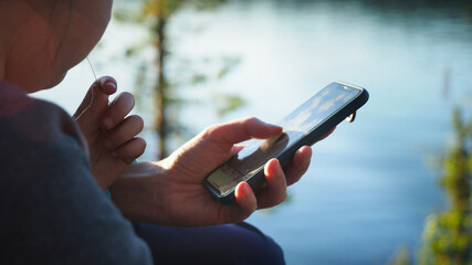 Close up. Mother using her mobile phone apps browsing chatting playing web surfing network with little daughter opposite the lake during sunset on spring camping vacation. Concept of modern technology