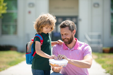 School lunch for kids. Father supports and motivates son. Schoolboy and parent in shirt holding lunch box.