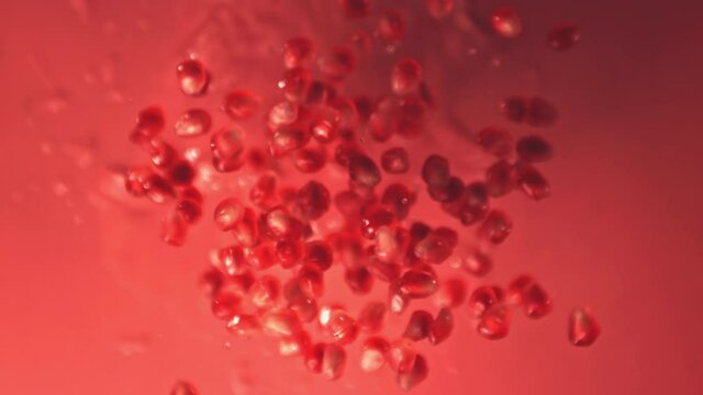 Super slow motion grain is a pomegranate with water droplets. On a red background. Filmed on a high-speed camera at 1000 fps. High quality FullHD footage