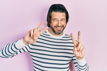 Fototapeta premium Middle age caucasian man wearing casual clothes smiling looking to the camera showing fingers doing victory sign. number two.