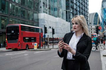 Young businesswoman wearing sunglasses is using her smartphone standing on the street.