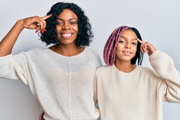 Beautiful african american mother and daughter wearing casual clothes and hugging smiling pointing to head with one finger, great idea or thought, good memory