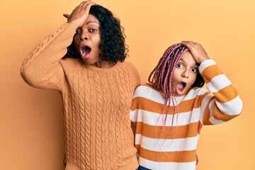 Beautiful african american mother and daughter wearing wool winter sweater surprised with hand on...