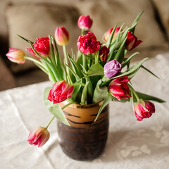 Obraz premium Colorful tulips in black vase on a white tablecloth