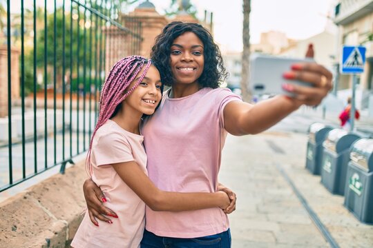 African american mother and daugther hugging and making selfie by the smartphone at the city.