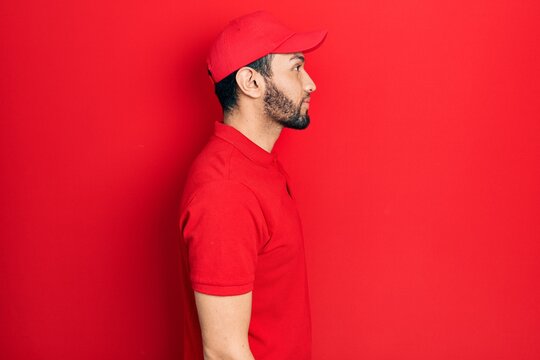 Hispanic Man With Beard Wearing Delivery Uniform And Cap Looking To Side, Relax Profile Pose With Natural Face And Confident Smile.