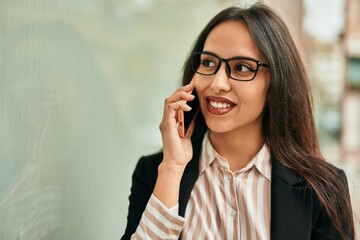 Young hispanic businesswoman smiling happy talking on the smartphone at the city.