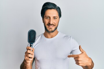 Young hispanic man styling hair using comb pointing finger to one self smiling happy and proud