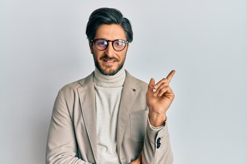 Young hispanic man wearing business jacket and glasses with a big smile on face, pointing with hand and finger to the side looking at the camera.