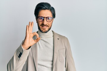 Young hispanic man wearing business jacket and glasses smiling positive doing ok sign with hand and...