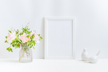 Mockup with a white frame, pink tulips and branches with green leaves in a vase on a light background
