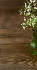 Delicate bouquet of white flowers in a small vase on a wooden background