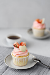 Cupcake with pink cream, strawberries and chocolate heart on a white plate on a light background