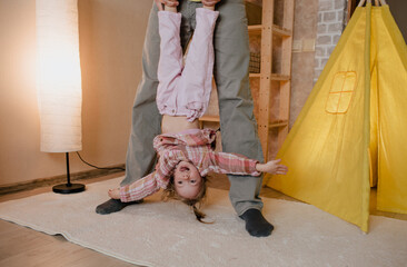 A father plays while holding his smiling daughter upside down in the room.