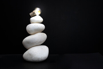 3 white stones stacked, with a lit light bulb, isolated on black background, macro