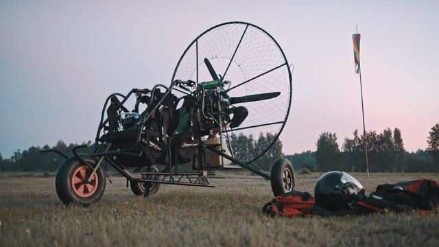 Low angle view on paramotor trike standing at grass, next to safety clothing and gear. Tandem motor powered paragliding at twilight. 