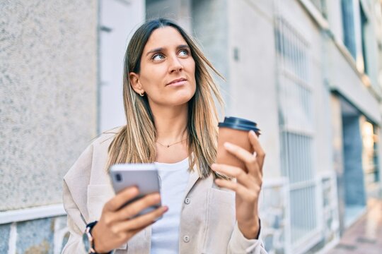 Young caucasian woman smiling happy using smartphone and drinking take away coffee at the city.