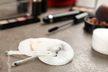 Dirty cotton pads, swabs and cosmetic products on grey table