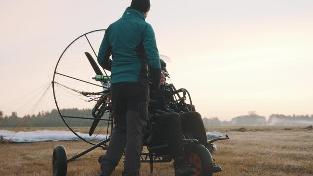 Pilot giving instructions to client before start. Walking around trike. Tandem motor powered paragliding at twilight. 