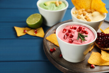 Bowl of delicious pink hummus with rosemary and pomegranate seeds on blue wooden table. Space for text