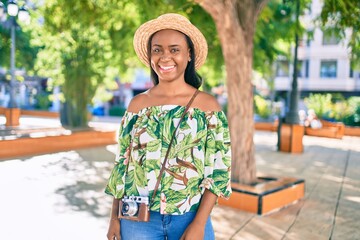 Fototapeta premium Young african american tourist woman on vacation smiling happy using vintage camera at the city.
