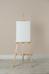 Wooden easel with blank canvas near beige wall