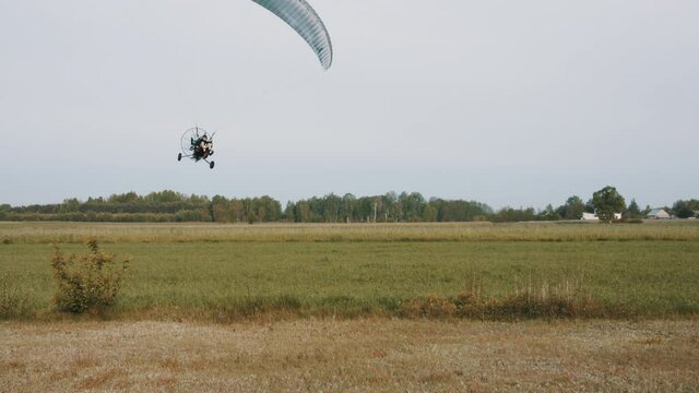 Low flight of paramotor trike above grass airport. Tandem motor powered paragliding at twilight. 