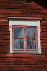 Obraz na płótnie Canvas Old window with peeling paint on a traditional Scandinavian red painted building. Spring tree branches reflecting in it