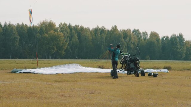 Instructor consistently checking parachute and cords before start. Tandem motor powered paragliding at twilight. 