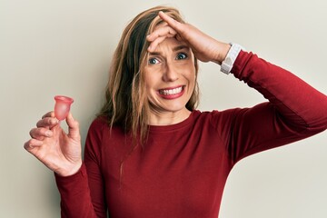 Young blonde woman holding menstrual cup stressed and frustrated with hand on head, surprised and angry face