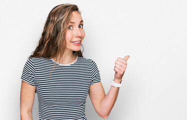 Young blonde woman wearing casual clothes smiling with happy face looking and pointing to the side with thumb up.