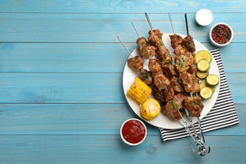 Metal skewers with delicious meat and vegetables served on light blue wooden table, flat lay. Space...