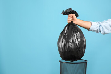 Woman taking garbage bag out of bin on light blue background, closeup. Space for text