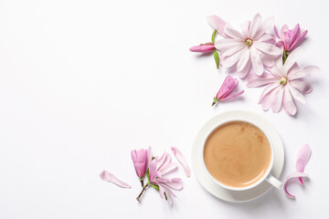 Beautiful pink magnolia flowers and cup of aromatic coffee on white background, top view