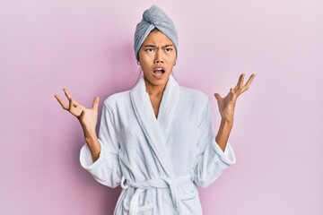 Young chinese woman wearing shower towel cap and bathrobe crazy and mad shouting and yelling with aggressive expression and arms raised. frustration concept.