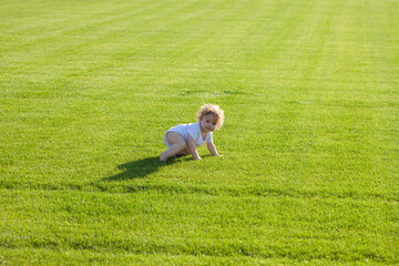 Fototapeta na wymiar Cute funny baby boy learning to crawl step, having fun playing on the lawn in the garden. Warm spring time in the park.
