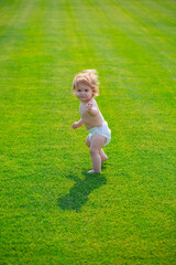 Cute funny laughing baby learning to crawl wearing a diaper having fun playing on the lawn watching summer in the garden. First step.