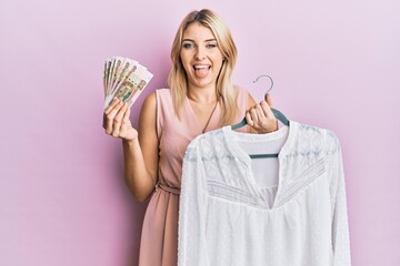 Young caucasian woman holding hanger with t shirt and russian ruble banknotes sticking tongue out happy with funny expression.