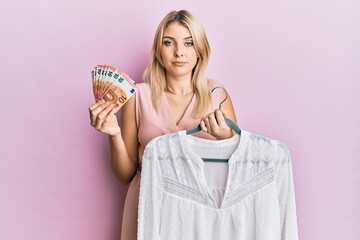 Young caucasian woman holding hanger with t shirt and euro banknotes depressed and worry for distress, crying angry and afraid. sad expression.