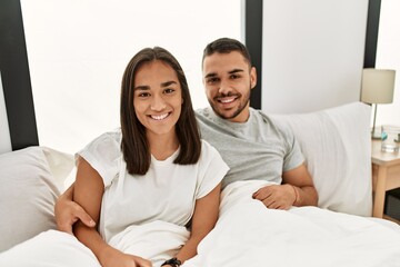 Fototapeta premium Young latin couple smiling happy hugging on the bed at home.
