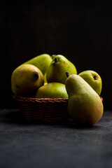Some fresh and green pears in a basket on a black wooden table 