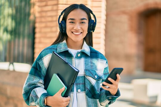 Young latin student girl smiling happy using smartphone and headphones at the city.