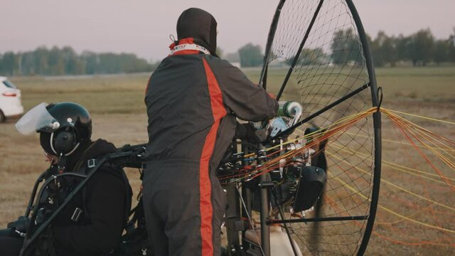 Man in flight overalls starting engine by start rope. Tandem motor powered paragliding at twilight. 