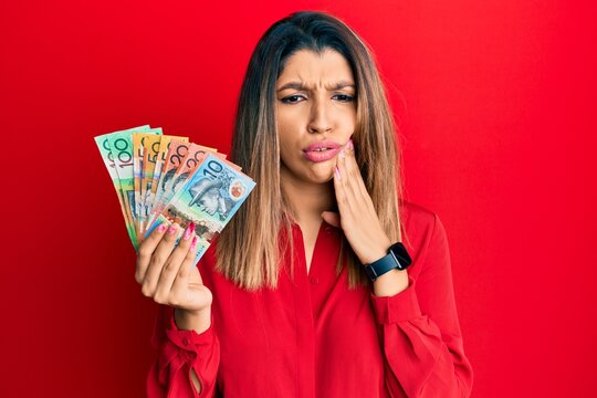 Beautiful brunette woman holding australian dollars touching mouth with hand with painful expression because of toothache or dental illness on teeth. dentist concept.