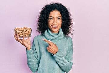 Young latin girl holding peanuts smiling happy pointing with hand and finger