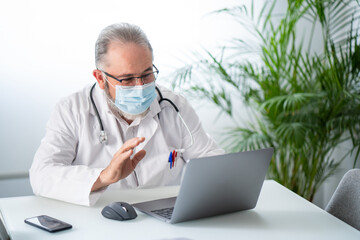 Senior doctor greeting in a video conference in a laptop with a patient. Telematic or online work concept.