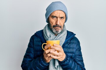 Middle age hispanic man wearing winter scarf and drinking a cup of hot coffee skeptic and nervous,...