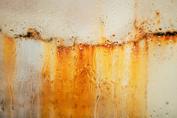 Streaks of rust on old metal behind dripping glass after rain.